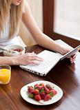 Blond woman using a laptop while having breakfast