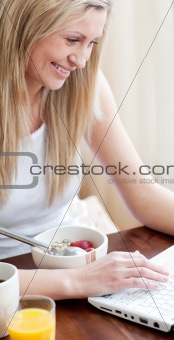 Cheerful woman using a laptop while having a breakfast