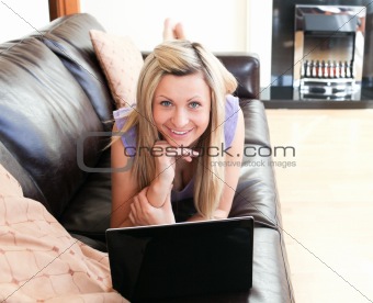 Smiling young woman using a laptop lying on a sofa
