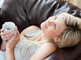 Charming woman drinking coffee sitting on a sofa