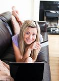 Smiling woman using a laptop lying on a sofa