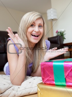 Astonished pretty woman opening gifts lying on the floor
