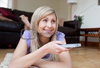 Joyful woman watching TV lying on the floor