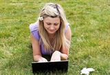 Charming young woman using a laptop lying on the grass