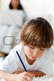 Concentrated little boy drawing lying on the floor 