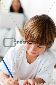 Merry little boy drawing lying on the floor in the living-room