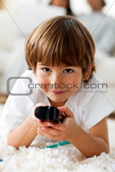 Smiling little boy holding a remote lying on the floor 