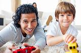 Cheerful father and his son playing video games lying on the flo
