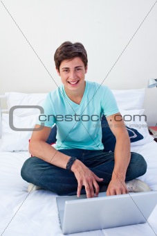 A teenage guy using a laptop in his bedroom