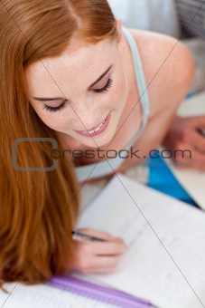Beautiful teenager doing homework on the floor