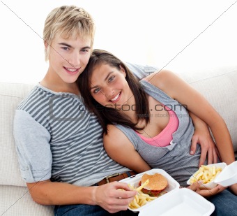 Teen couple eating burgers and fries at home