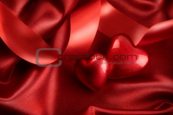 Two red hearts with ribbon on satin 