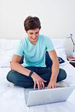 A teenage guy sitting on his bed using a laptop