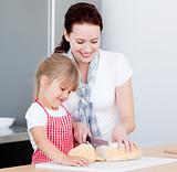 Mother teaching daughter how to cut bread in kitchen