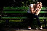 sad young woman sitting on bench in park