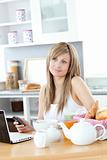 Cheerful woman using a phone and laptop in the kitchen