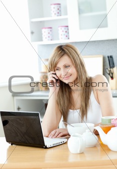 Delighted woman using a laptop in the kitchen
