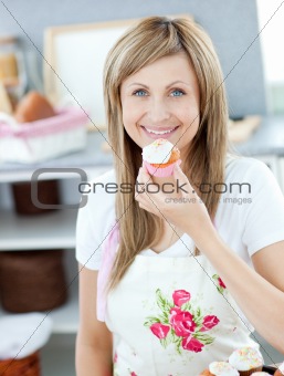 Delighted woman eating a little cake in the kitchen 