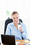 Smiling businesswoman holding a coffee while using a laptop 