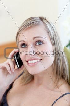 Smiling young woman sending a text lying on a sofa at home