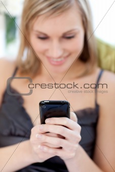 Young woman sending a text sitting on a sofa 