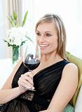 Happy woman drining red wine sitting on a sofa