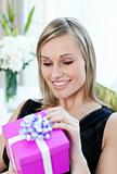 Happy woman opening a gift sitting on a sofa 