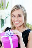 Glowing woman opening a gift sitting on a sofa 