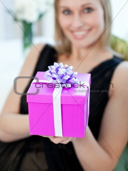 Blond woman opening a gift sitting on a sofa