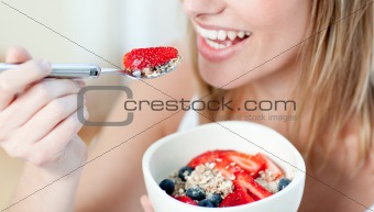 Charming woman eating muesli with fruits sitting on a sofa
