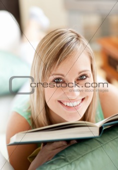 Radiant woman lying on a sofa reading a book