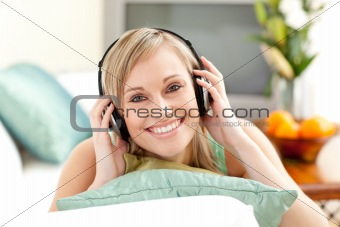 Happy blond woman listening music lying on a sofa