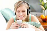 Smiling blond woman listening music lying on a sofa 