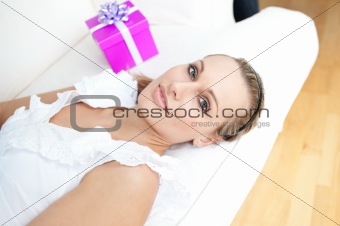 Beautiful blond woman with a present lying on a sofa 