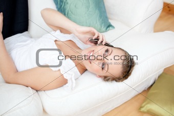 Radiant young woman talking on phone lying on a sofa