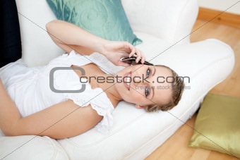 Bright young woman talking on phone lying on a sofa
