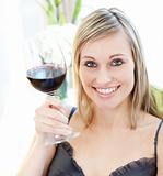 Beautiful blond woman drining red wine sitting on a sofa