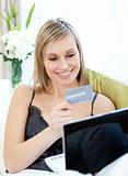 Attractive blond woman shopping on-line sitting on a sofa