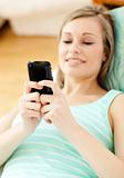 Bright young woman sending a text lying on a sofa 
