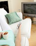 Attractive woman drinking a coffee while watching TV lying on a sofa