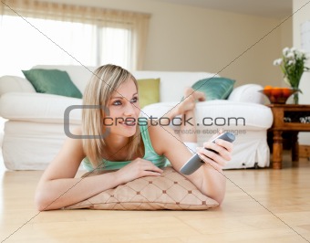 Beautiful blond woman watching TV lying on the floor 
