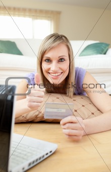Jolly woman shopping online lying on the floor in a living-room