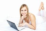 Cheerful woman using a laptop lying on her bed 
