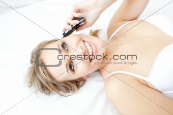 Laughing woman talking on phone lying on her bed