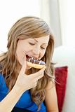 Radiant woman is eating a donut on a sofa 