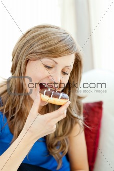 Radiant woman is eating a donut on a sofa 