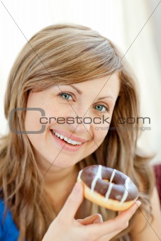 Smiling woman is eating a donut on a sofa 