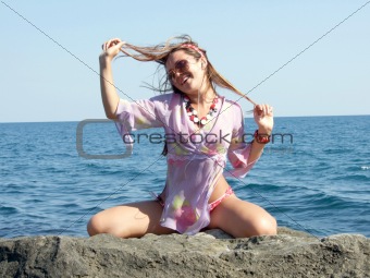 The sexual girl sits on a stone on a background of the sea