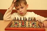 The boy plays a chess behind a table