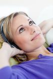 Cheerful young woman listening music lying on a sofa in the living-room